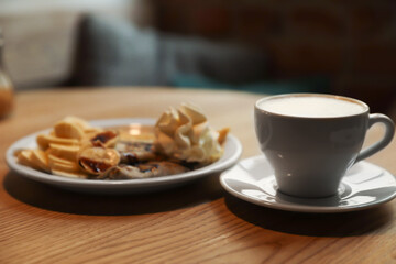 Cup of aromatic coffee and delicious desserts on wooden table indoors
