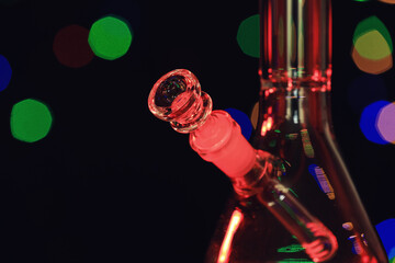 Closeup view of glass bong against blurred lights. Smoking device