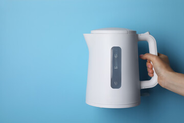 Woman holding modern electric kettle on light blue background, closeup. Space for text