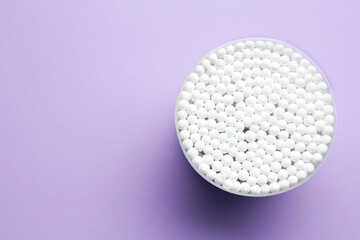 Many cotton buds in container on violet background, top view. Space for text