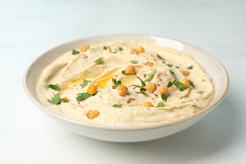Tasty hummus with garnish in bowl on white table, closeup
