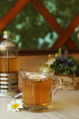Tasty herbal tea and fresh chamomile flowers on white table