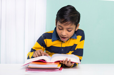 Indian boy reading book over study table at home