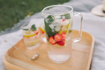 Glass jug of lemonade with berries on the beach.Summer Picnic. Homemade delicious drinks.