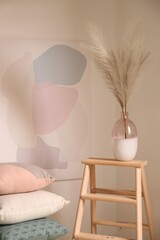 Vase with decorative dried plants and painting in stylish room interior