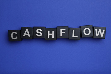 Black wooden cubes with phrase Cash FLow on blue background, flat lay