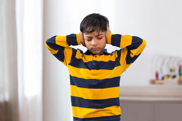 An Indian boy closed eyes covering ears with hands