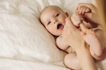 mother playing with a cute little smiling baby. Mom touches a cute baby in a diaper while having a...