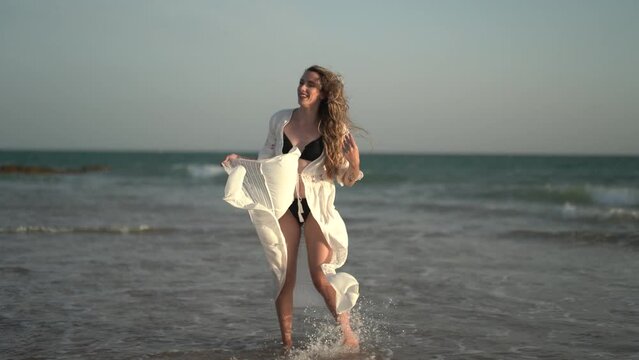 Chica joven en la playa posando y riendo al atardecer en la orilla del mar