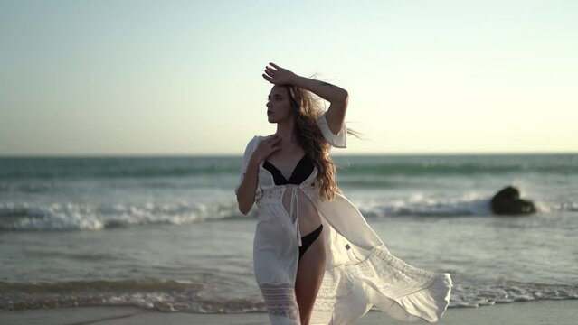Chica joven en la playa posando y riendo al atardecer en la orilla del mar