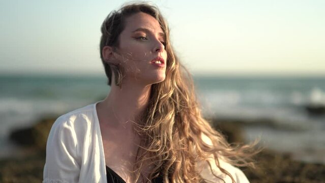 Chica joven en la playa posando y riendo al atardecer en la orilla del mar