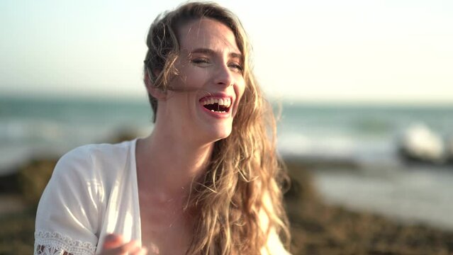 Chica joven en la playa posando y riendo al atardecer en la orilla del mar