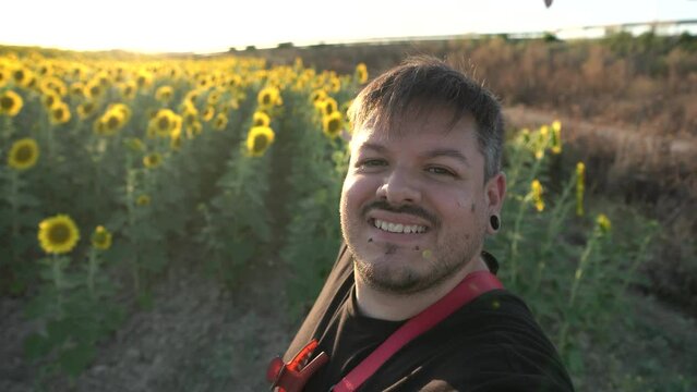 Chico gordo con barba de tres d&iacute;as grab&aacute;ndose modo selfie en un campo de girasoles