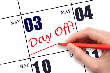 Hand writing text DAY OFF and drawing a line on calendar date 3 May. Vacation planning concept.