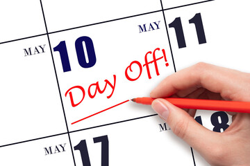 Hand writing text DAY OFF and drawing a line on calendar date 10 May. Vacation planning concept.
