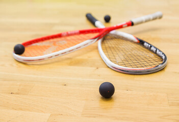 Two rackets and squash balls lie on the parquet floor