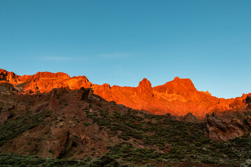 Scenic view on rock formations during sunrise near volcano Pico del Teide, Mount Teide National Park, Tenerife, Canary Islands, Spain, Europe. First sunbeams touching mountain peaks turning fire red