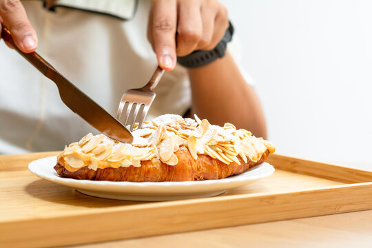 Desert and sweet bakery concept. Eating croissant almonds with a knife and frok on a white plate in cafe and coffee shops.