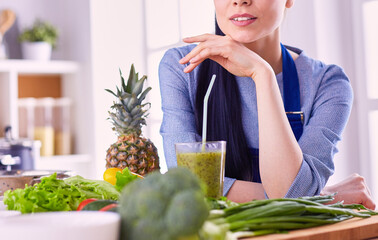 Young woman with glass of tasty healthy smoothie at table in kitchen