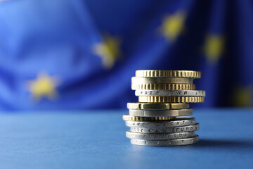 Stack of coins on blue table against European Union flag, closeup. Space for text