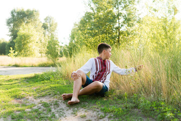 Portrait of a teenager boy in Ukrainian traditional national clothes - vyshyvanka on a green background. Ukraine, child in nature