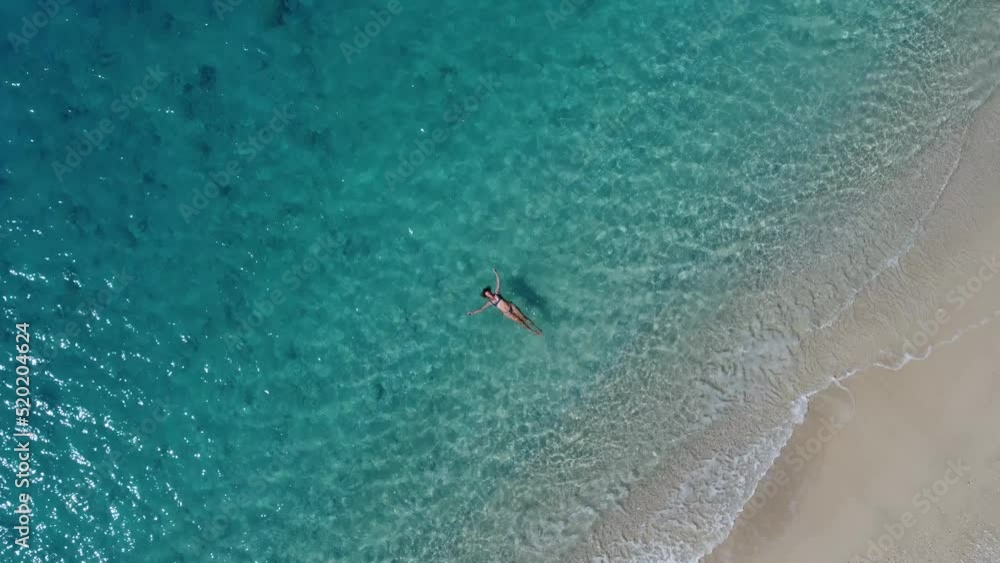 Wall mural aerial view of beautiful happy woman in swimsuit laying in the shallow sea water, enjoying sandy bea