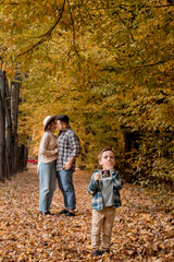 Naklejka premium Happy family of a man with a woman and surprised son holding an ultrasound pregnancy picture. Autumn photo shoot of a family waiting to be replenished