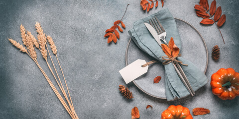 Autumn table setting on grunge gray background. Gray plate, cutlery and decorative pumpkins. Thanksgiving and harvest concept. Top view, flat lay. Selective focus, banner