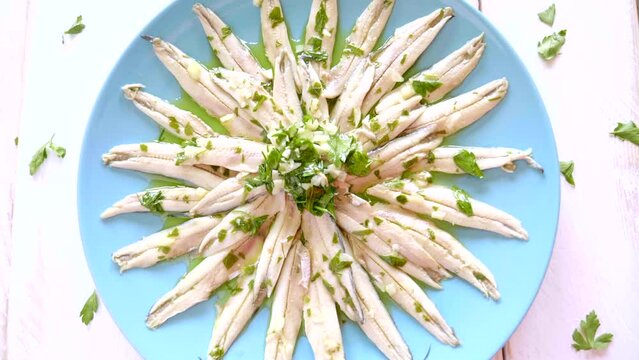 Pickled anchovies with garlic and parsley marinated in vinegar in a round wooden plate on a white wooden table. Typical Spanish snack. 