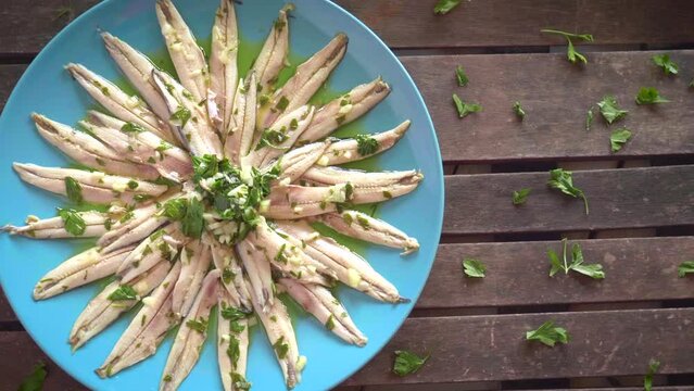 Pickled anchovies with garlic and parsley marinated in vinegar in a round blue plate on a dark wooden table. Typical Spanish snack.