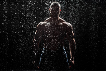 Muscular man under the rain in studio. Sexy male in water drops