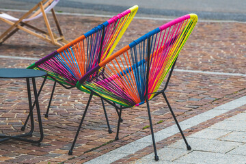 Two colorful Acapulco style chair in rainbow colors and a little table at a cafe in a street