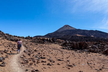 Woman with backpack on volcanic desert terrain hiking trail leading to summit volcano Pico del Teide, Mount Teide National Park, Tenerife, Canary Islands, Spain, Europe. Solidified lava, ash, pumice