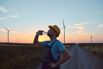 Silhouette of an engineer mechanic in a windmill farm park drinking water after hard working day.