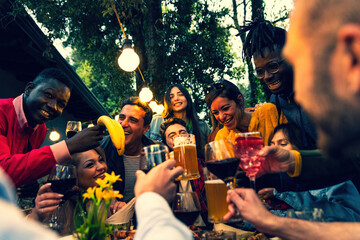 Multiracial People holding glasses of wine and beer making a toast – multi ethnic friends clinking glasses of wine and beer – cheerful friends clinking glasses above dinner table