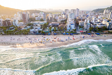 Imagem aérea da praia do Tombo, localizada na cidade do Guarujá. Ondas, natureza, montanhas e banhistas.