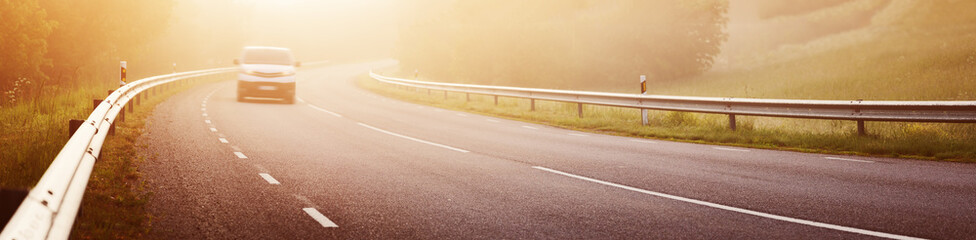 Fototapeta premium Black asphalt road with dividing line and safety fence in the morning mist.