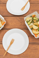 Picnic using reusable dishes. Barbecue in the company, outdoor barbecue. Takeaway food in container. Grilled vegetables. Eating outdoor on wooden table. Table ware flat lay.
