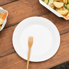 Picnic using reusable dishes. Barbecue in the company, outdoor barbecue. Takeaway food in container. Eating outdoor on wooden table. One fork and one dish.