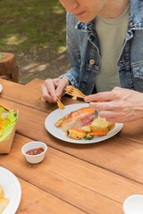 Salmon grilled fish with grilled vegetables in eco disposable tableware. Grilled potato, carrot, vegetable marrow. Man 
eating fish. Picnic in park. Vertical photo. Outdoor picnic in sunny day.