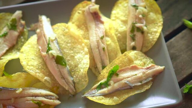 Potato chips with pickled anchovies in a dark rectangular plate on a dark brown wooden table. Typical Spanish food to eat in a bar.