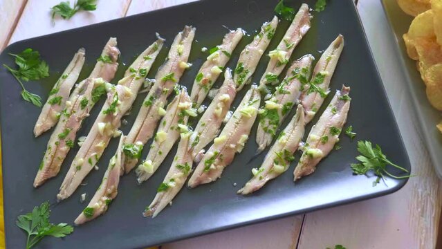 Three dishes with potato chips, picked anchovies and green olives on a white wooden table with parsley leaves. Typical Spanish snacks to eat in a bar.