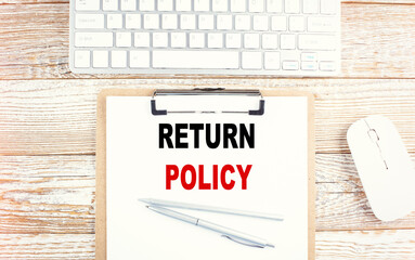 RETURN POLICY text on clipboard with keyboard on wooden background