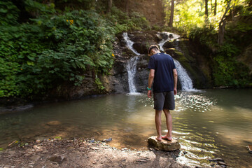 man stands near a waterfall in the middle of the forest