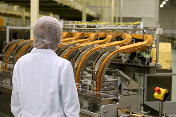 A woman controls the production process. Large biscuit factory. A line of biscuits in a large factory. Packing crackers on the machine.