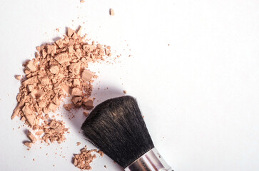 Scattered cosmetic powder of natural beige shade and makeup brush on white background with copy space