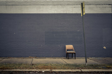 Single chair sitting against a brick wall behind a bustop