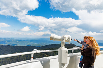 Mother shows son landscapes in valley of Rhodope Mountains and sky through telescope on observation tower of Snezhan