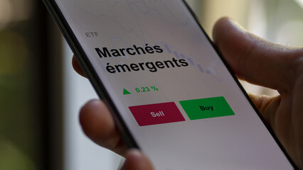 Un investisseur analyse un fonds etf marchés émergents sur un graphique. Un téléphone affiche le cours de l'ETF. Texte en français francais Marchés émergents
