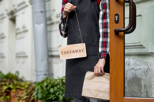 woman holds a wooden sign with the inscription takeaway, open or closed at the door of a restaurant or coffee shop. the working hours of the restaurant or the food and beverage delivery service. to